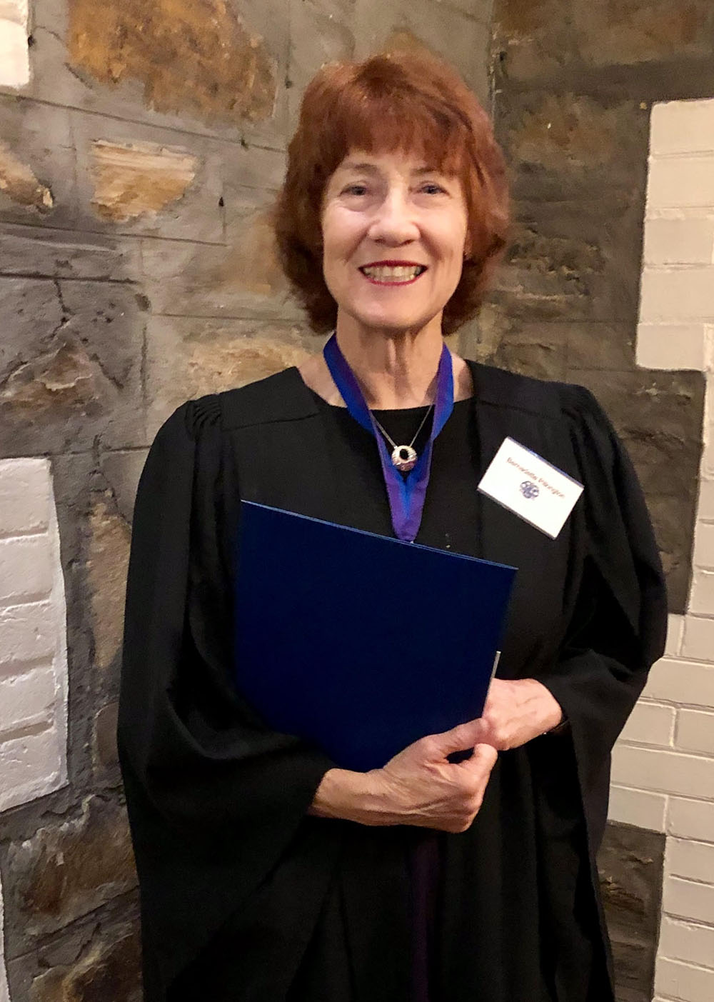 Bernadette standing in a black university gown with a medal on and an award on hand.