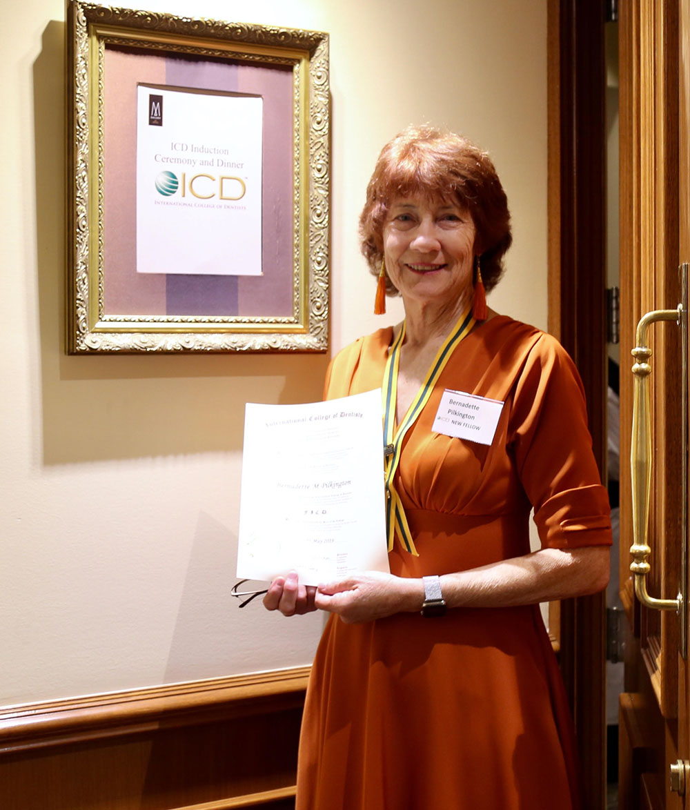 Bernadette standing in front of a framed and mounted certificate.