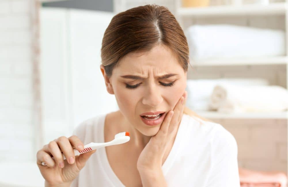 Woman experiencing pain while brushing teeth.