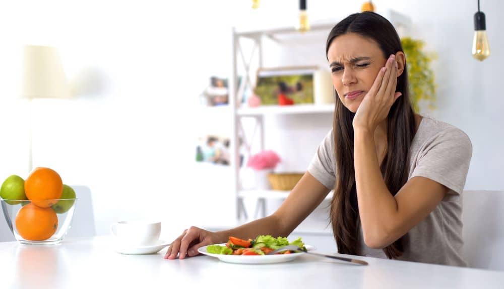 Woman experiencing tooth pain while eating. 