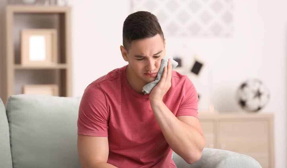 Young man applying cold compress to cheek.