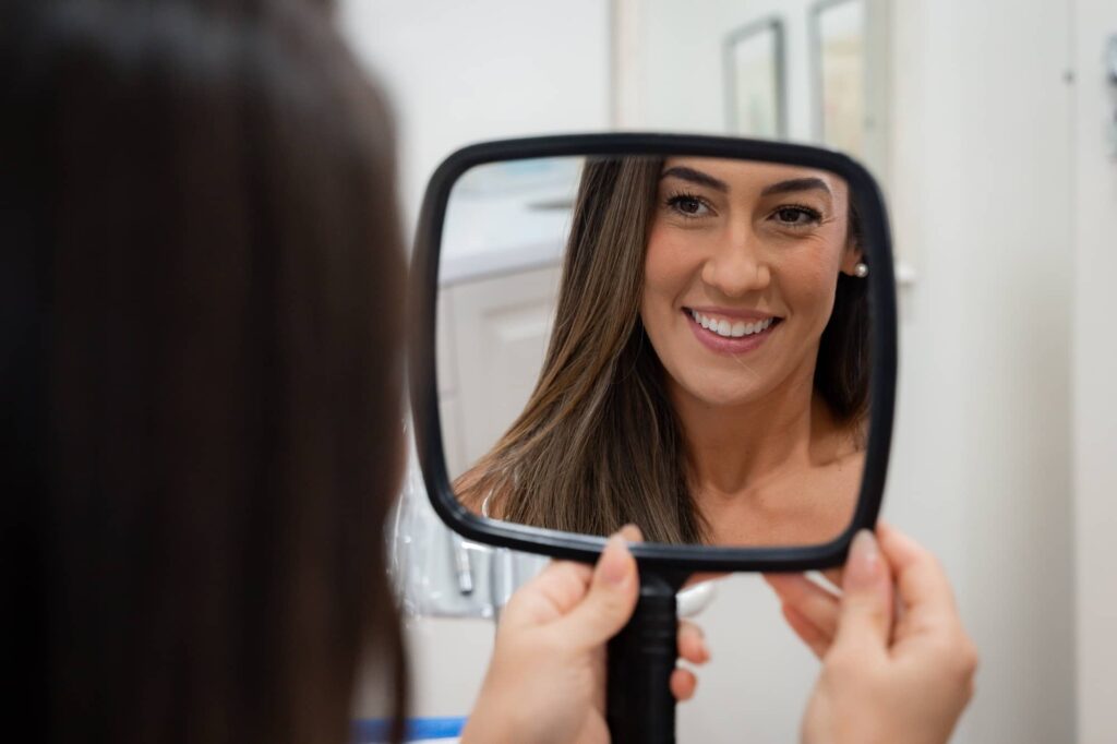 Lady smiling in mirror showing her porcelain veneers