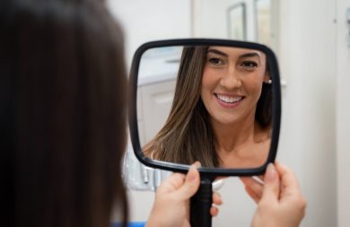 Lady smiling in mirror showing her porcelain veneers