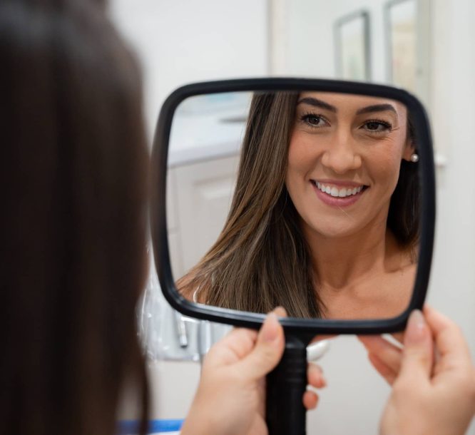 Lady smiling in mirror showing her porcelain veneers