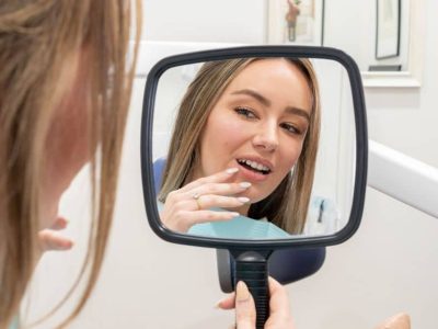 Woman holding a mirror checking her teeth.