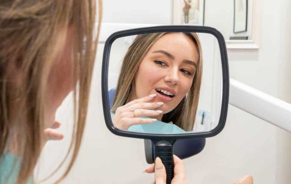 Woman holding a mirror checking her teeth.