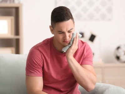 Young man applying cold compress to cheek.