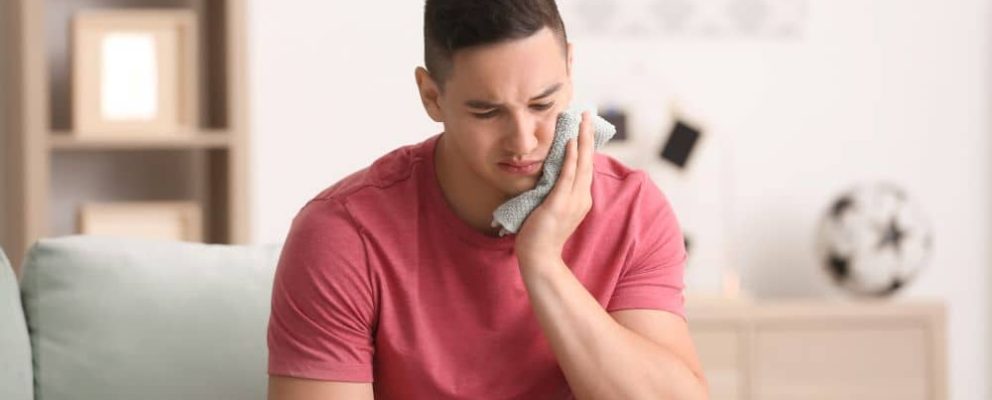 Young man applying cold compress to cheek.