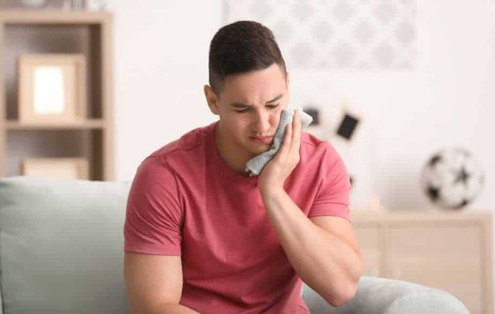 Young man applying cold compress to cheek.