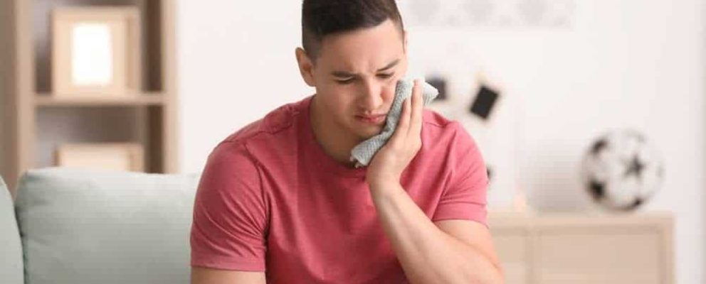 Young man applying cold compress to cheek.