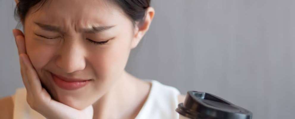 Woman with sensitive tooth experiencing pain while drinking coffee.